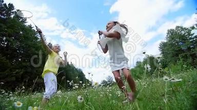 在绿色的洋甘菊草坪上，女孩，孩子，<strong>打羽毛球</strong>，。 他们跑，跳，到处乱跑。 他们玩得很开心。 夏季